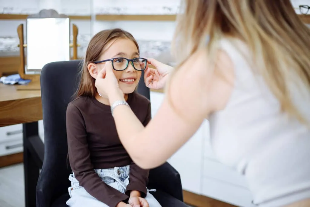 Young girl trying on eyeglasses with assistance from an eye care professional
